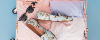 Valise remplie pour les vacances avec des t-shirts, des lunettes de soleil et des chaussures fleuries