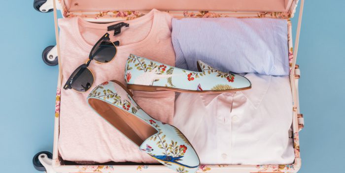 Valise remplie pour les vacances avec des t-shirts, des lunettes de soleil et des chaussures fleuries