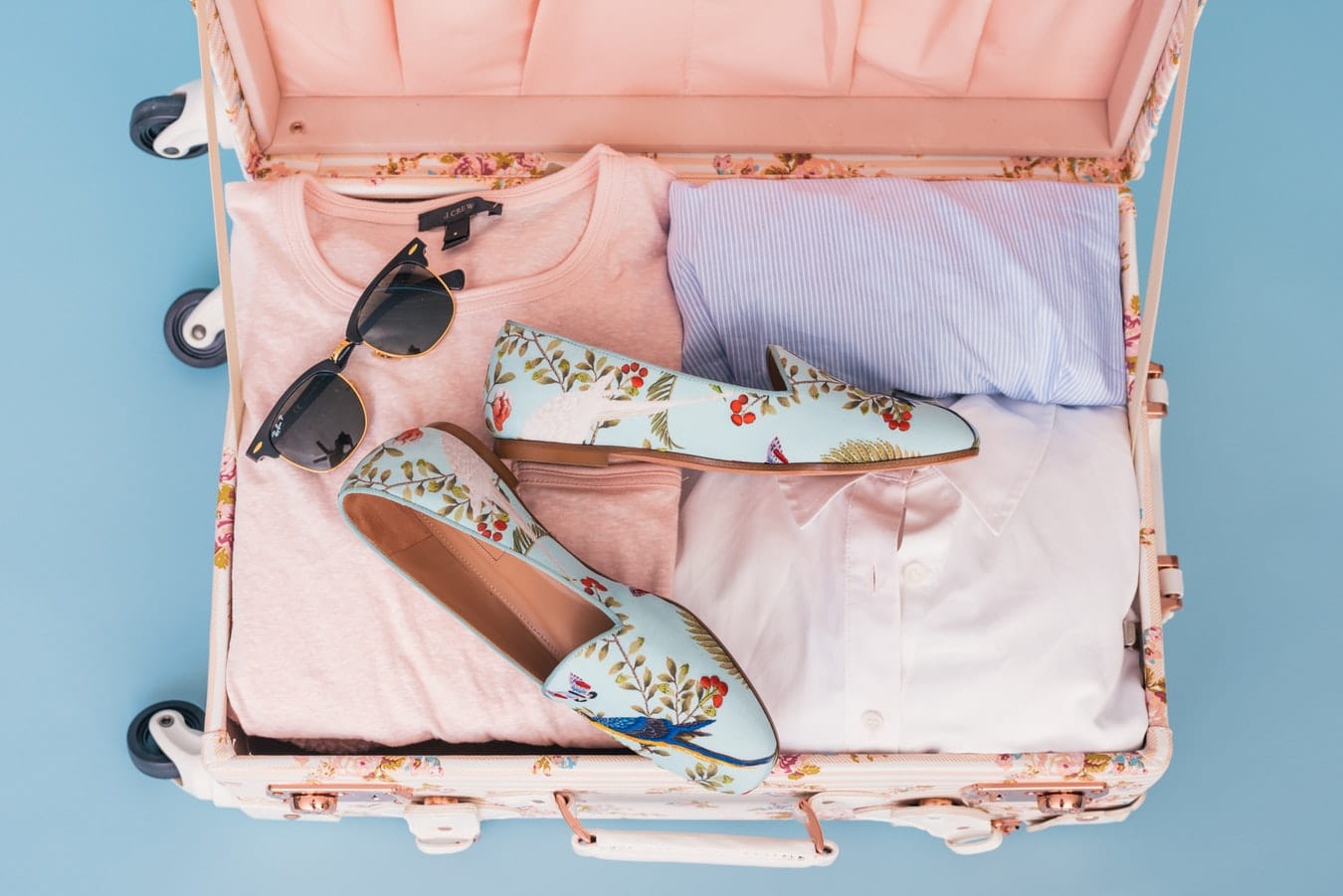 Valise remplie pour les vacances avec des t-shirts, des lunettes de soleil et des chaussures fleuries